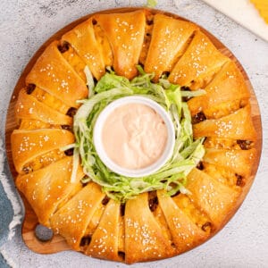 square image of a cheeseburger crescent roll ring on a round wooden tray