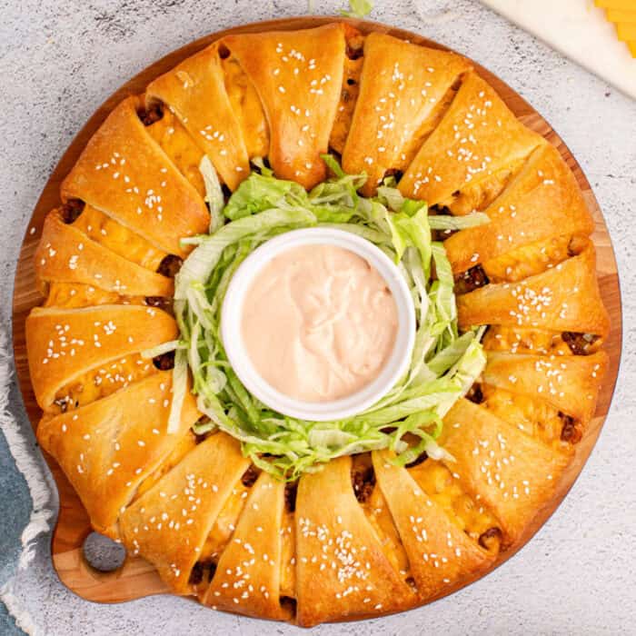 square image of a cheeseburger crescent roll ring on a round wooden tray