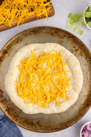 shredded cheddar cheese spread over pizza crust