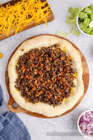 cooked bground beef and crumbled bacon over shredded cheddar on a pizza crust