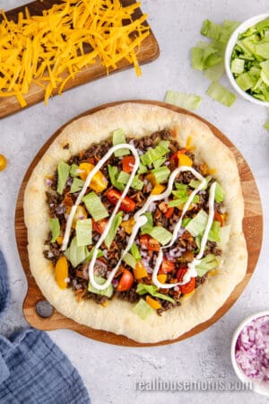 mayonnaise drizzled over a cheeseburger pizza in a zig-zag pattern