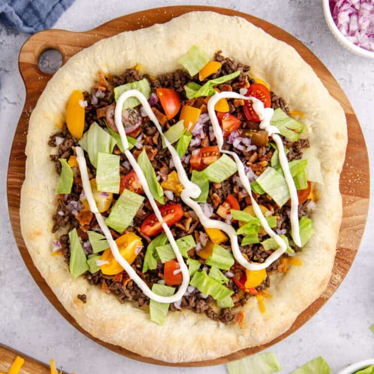 square image of a whole cheeseburger pizza on a wooden platter