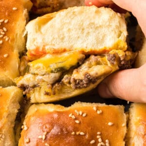 square image of a hand taking a cheeseburger slider from the pan