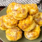 square image of cheesy bacon & egg muffins piled on a plate
