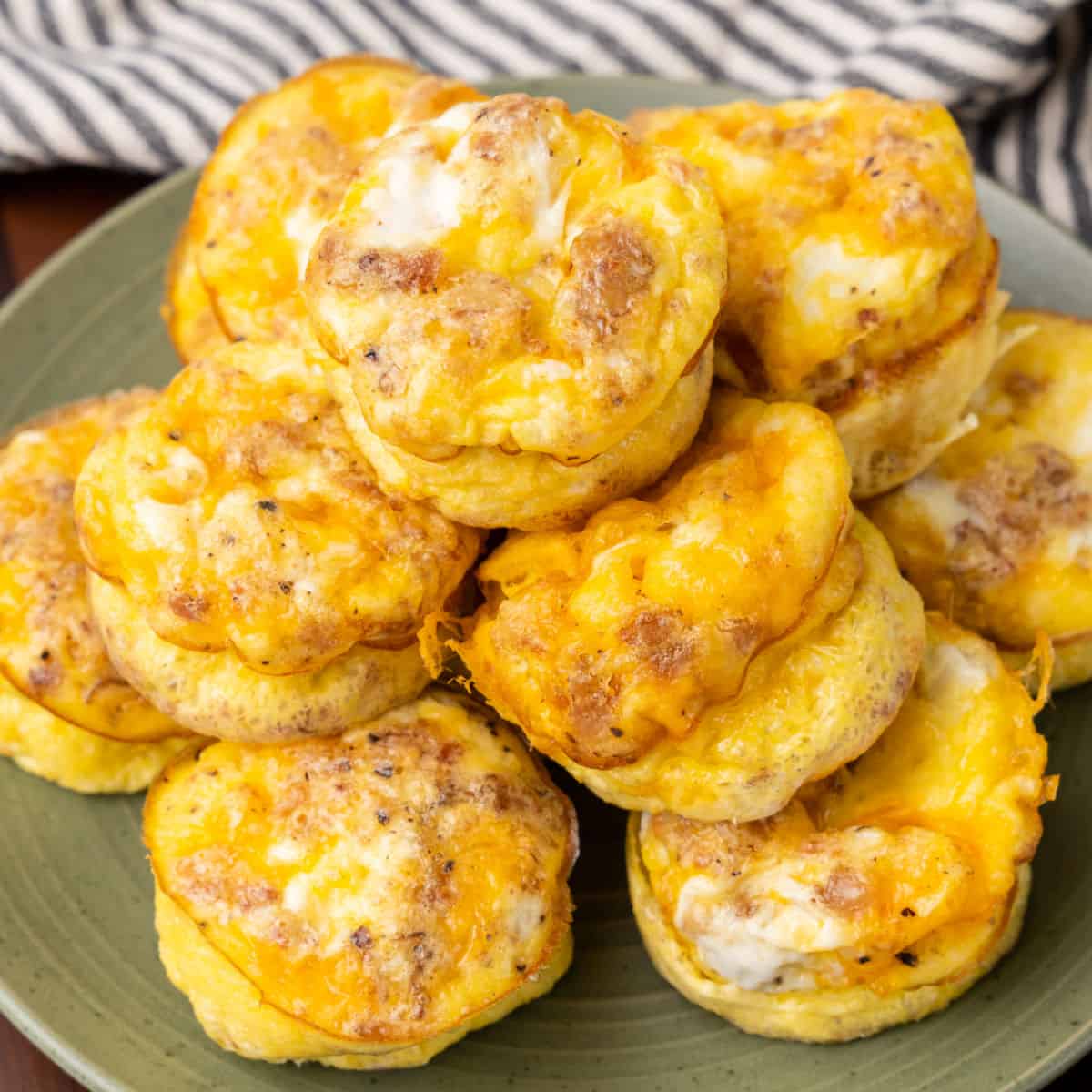 square image of cheesy bacon & egg muffins piled on a plate