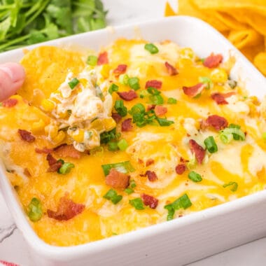 square image of a tortilla chip fo being dipped into cheesy bacon & roasted corn dip
