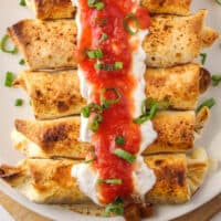 beef taquitos on a plate with sour cream, salsa and green onion on top with recipe name at the bottom