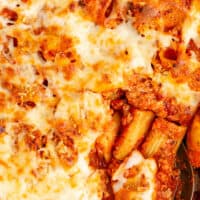 picture of cheesy baked rigatoni in a baking dish after cooking with a spoon on the bottom right with the title of the post on the top in blue and black lettering