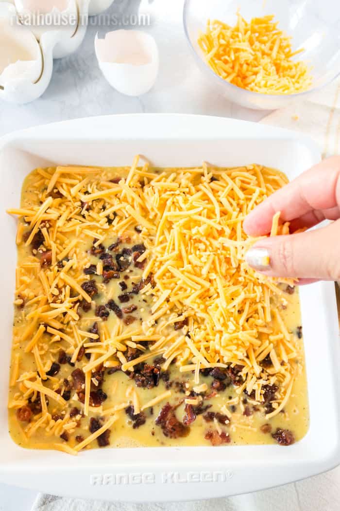 cheese being sprinkled onto a breakfast casserole