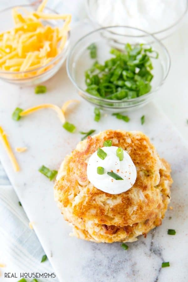 Cheesy Cauliflower Pancakes with cheese, green onions, and sour cream near by, ready to garnish