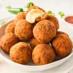 square image of a pile of cheesy mexican rice balls with the top one broken open
