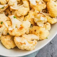 cheesy roasted cauliflower in a white serving bowl wtih recipe name at the bottom