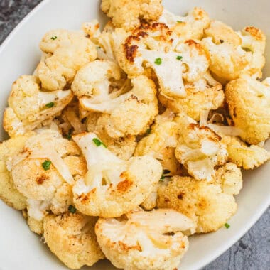 square image of cheesy roasted cauliflower on a white serving dish