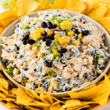 square image of cheesy roasted corn and black bean dip in a bowl surrounded by tortilla chips