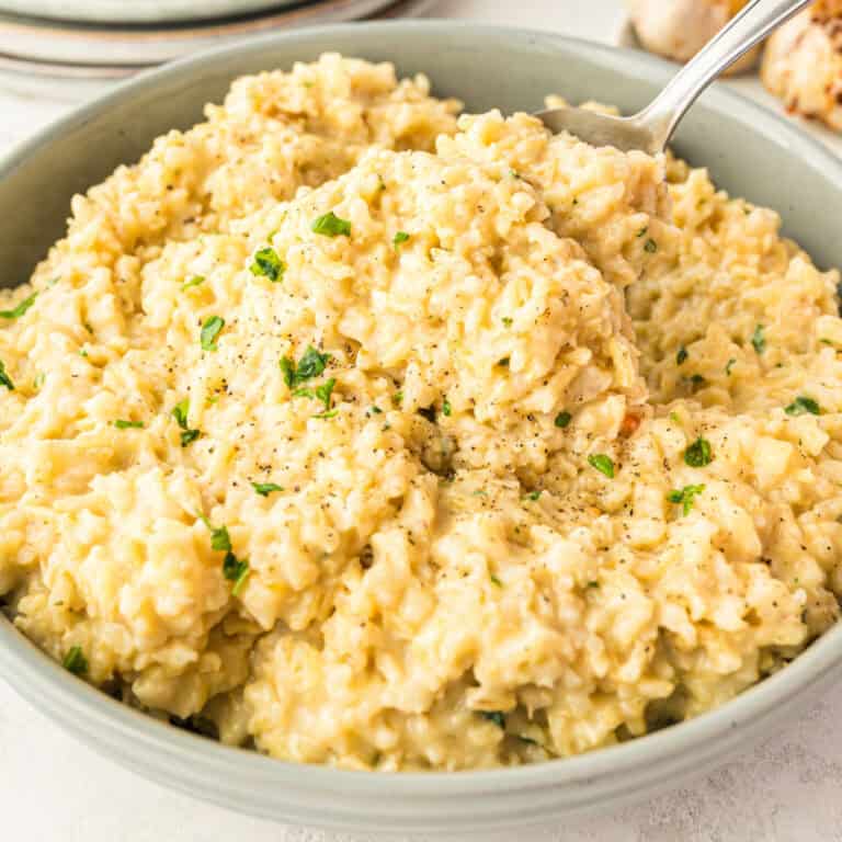 square image of a spoonful of cheesy roasted garlic rice over the serving bowl