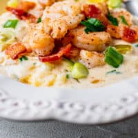 bowl of shrimp and grits tipped with green onion, bacon, and a lemon slice with recipe name at bottom