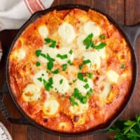 square image of cheesy skillet ravioli bake topped with chopped parsley