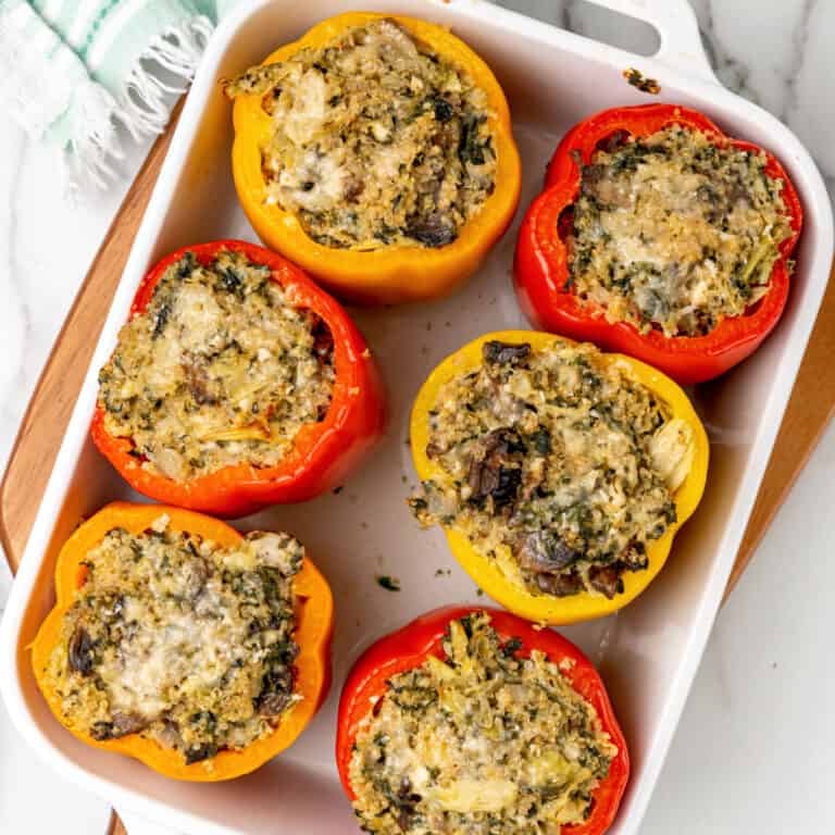 square image of cheesy spinach and artichoke quinoa stuffed peppers in a baking dish