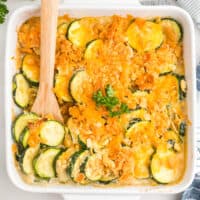 square image of cheesy zucchini gratin in a baking dish with a wooden spoon