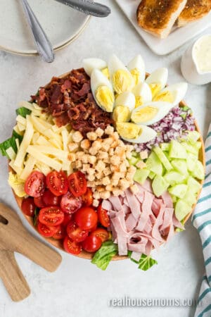 chef salad ingredients arranged in sections over chopped lettuce in a large wooden bowl