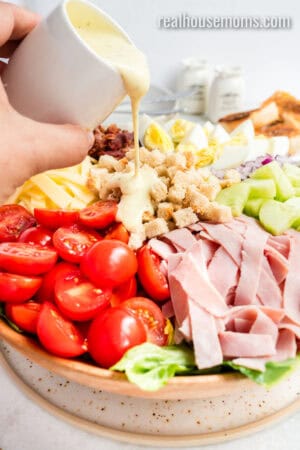 salad dressing being poured over chef salad in a large wooden bowl