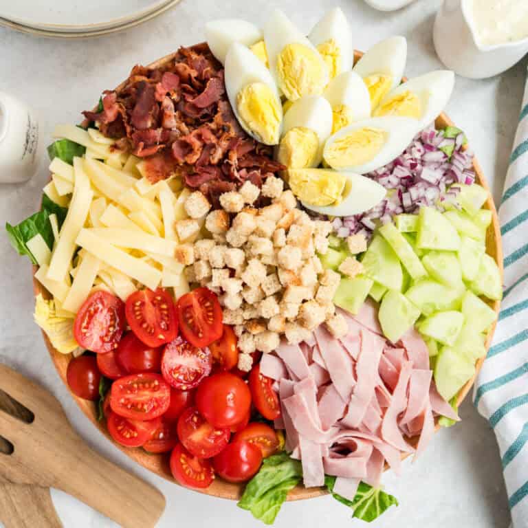 square image of chef salad in a serving bowl with the toppings arranged in sections