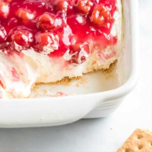white baking dishe with cherry cheesecake dip missing dip in the corner to reveal graham cracker crust
