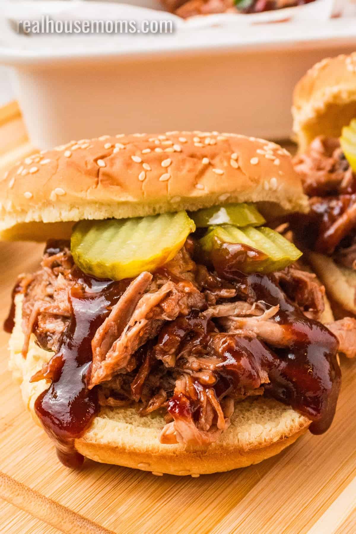 close up of a cherry cola pulled pork sandwich with extra bbq sauce and pickle slices