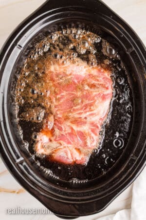 seasoned pork shoulder in a slow cooker filled with cherry cola
