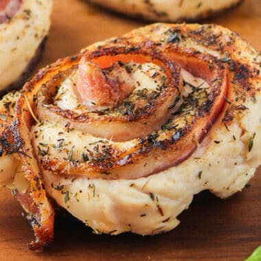 square close up image of a bacon chicken roll up on a wooden plate