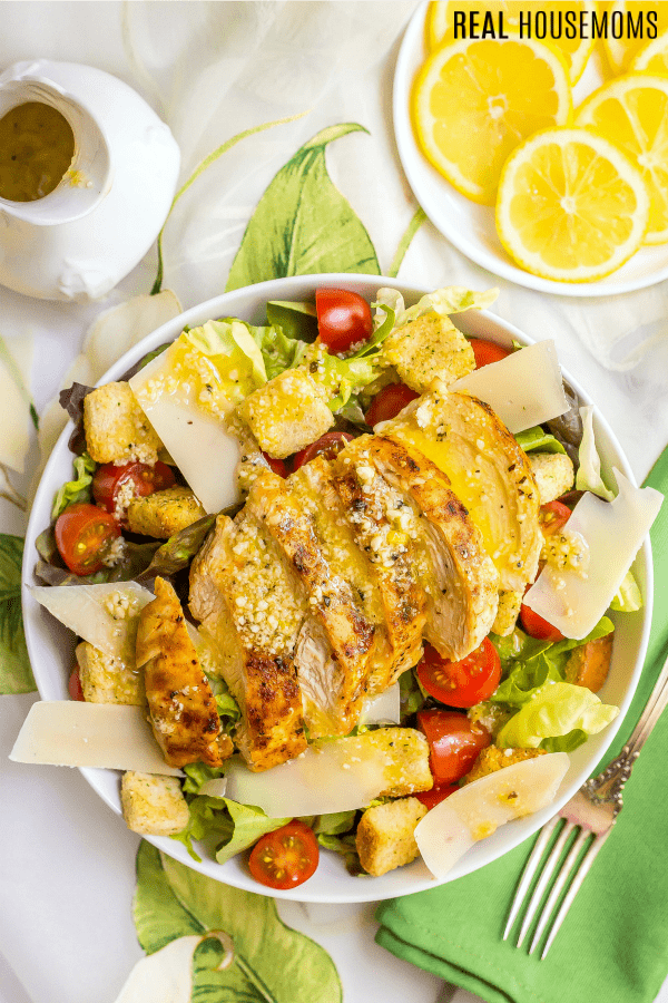 overhead photo of chicken caesar salad with a plate of lemon slices on the side