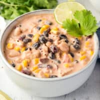 square imgae of a bowl of chicken chili with parsley and lime wheel for garnish