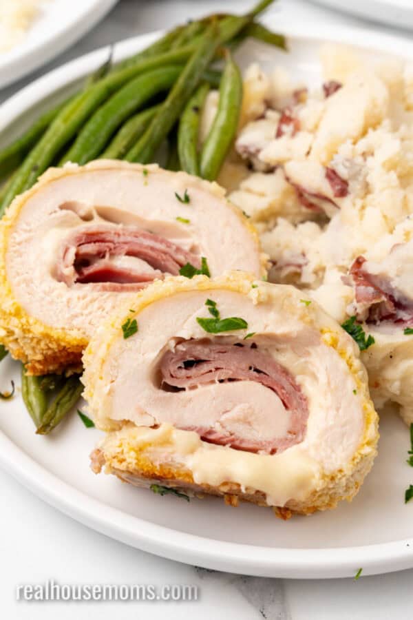 close up of chicken cordon bleu slices with dijon sauce on a dinner plate with sides