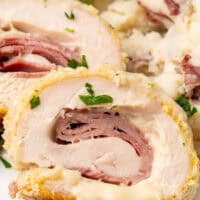 image of of chicken cordon bleu slices on a dinner plate with sides with the title of the post on top in blue and black lettering