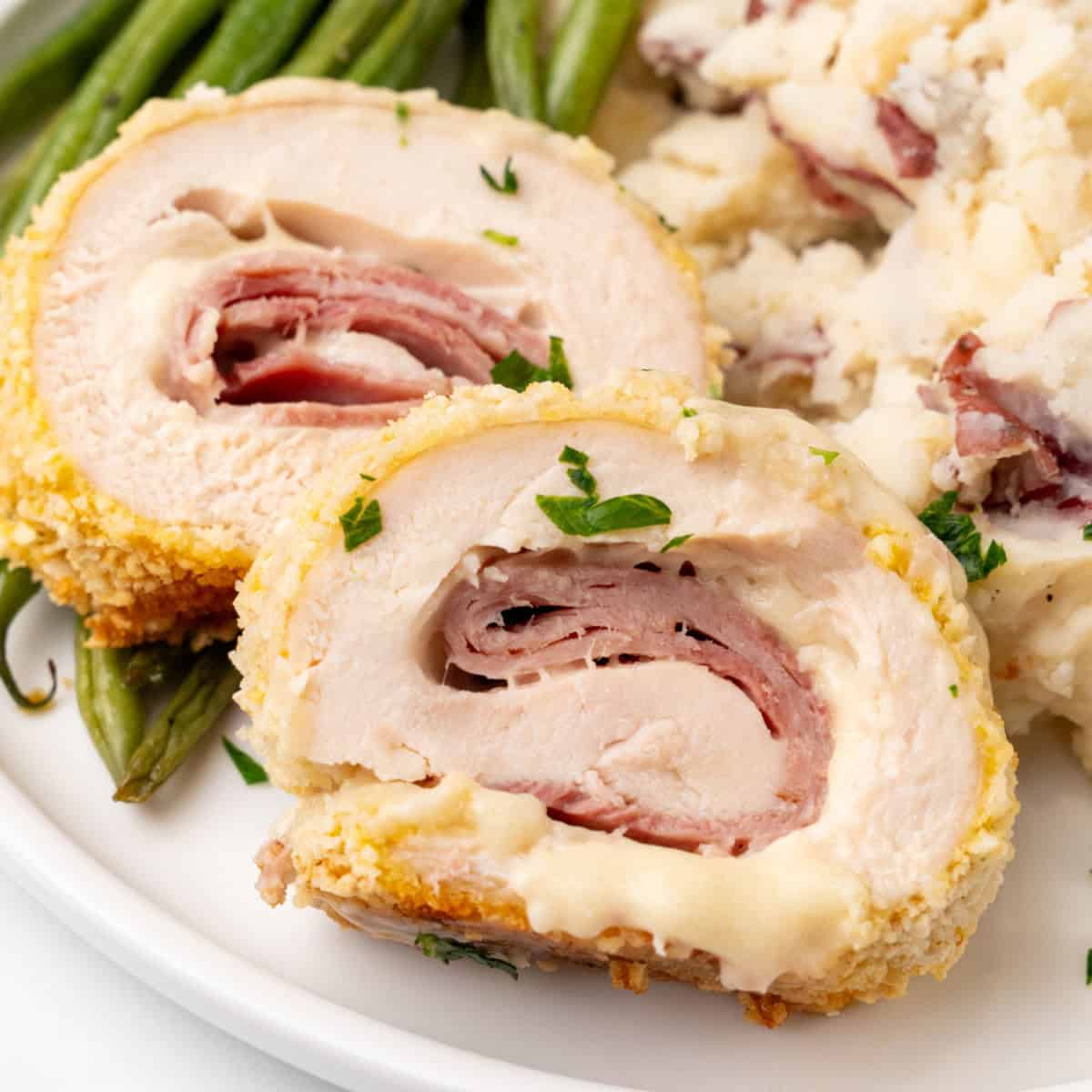 square image of chicken cordon bleu slices on a dinner plate with sides