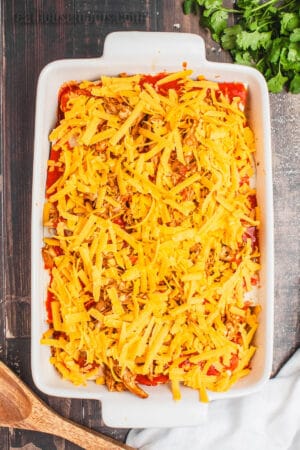 layered Chicken Enchilada Casserole topped with shredded cheddar cheese in a baking dish before cooking