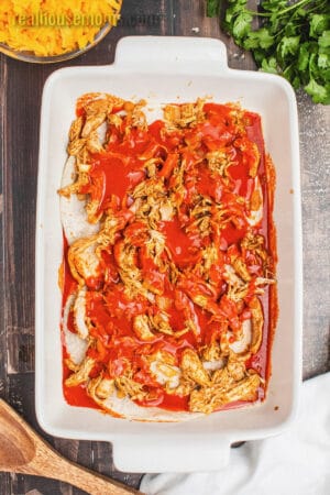 tortillas layered with seasedon shredded chicken and enchilada sauce in a baking dish