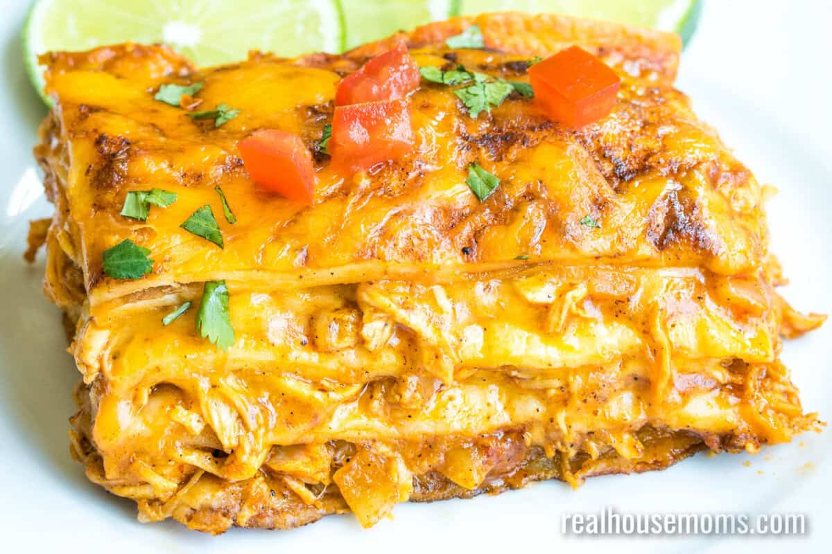 portion of chicken enchilada casserole on a white plate with lime wedges