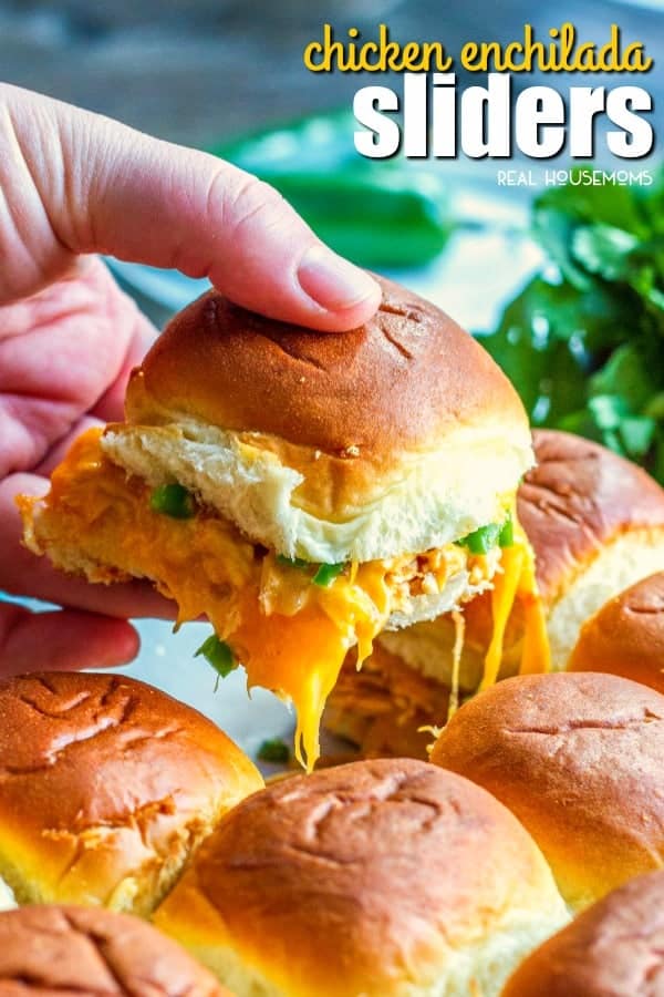 Hand lifting a Chicken Enchilada Slider out of the baking dish with lots of gooey cheese pulling long with the sandwich