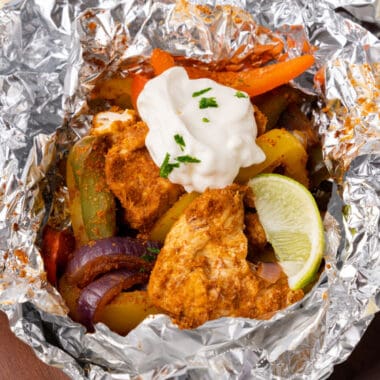 square image of a chicken fajita foil pack topped with sour cream, cilantro, and a lime wedge
