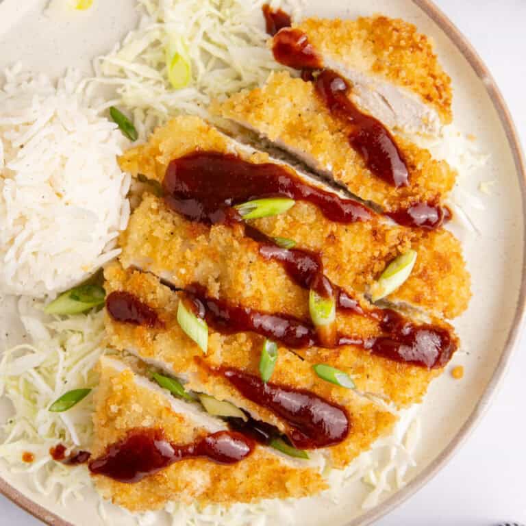 square image of chicken katsu on a plate with a side of rice with sauce on top