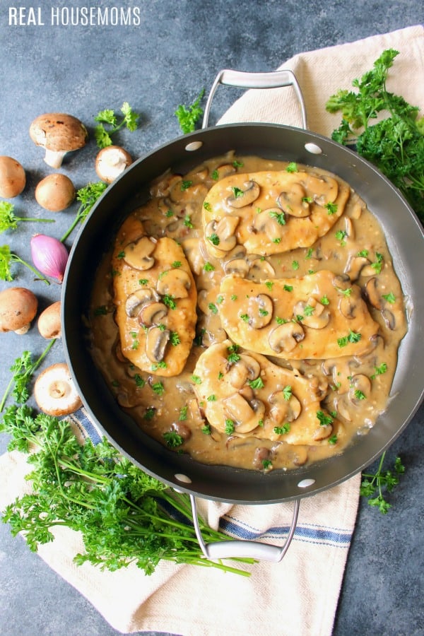 looking down at a skillet of chicken marsala with prsely and veggies on the counter next to the skillet