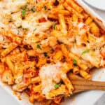 square image of chicken parmesan baked ziti in a dish with with a portion on a wooden spoon