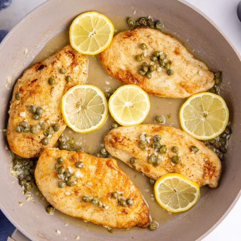 square image of chicken picatta on a grey serving plate either lemon wedges for garnish