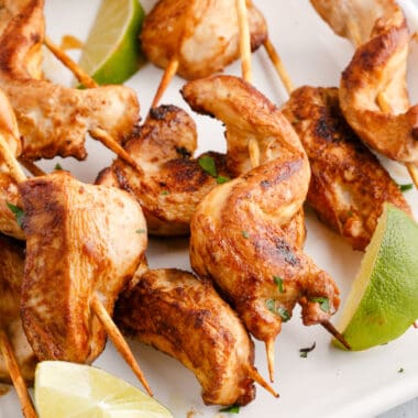 square image of chicken satay skewers with parsley and lime wedges