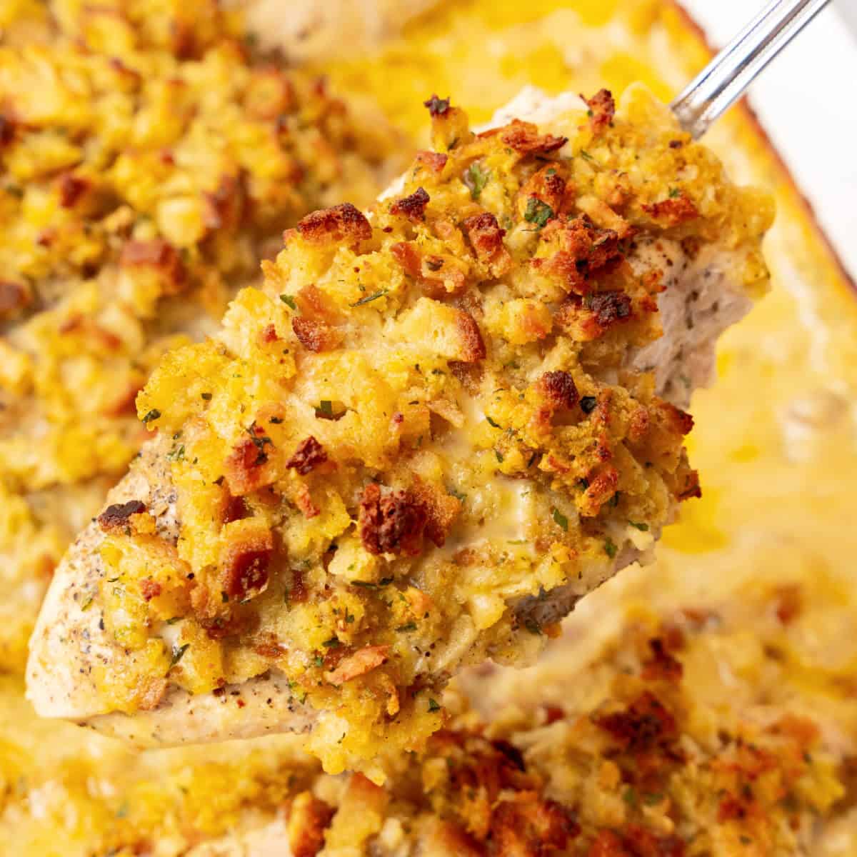 square image of chicken stuffing bake on a serving spoon over the baking dish