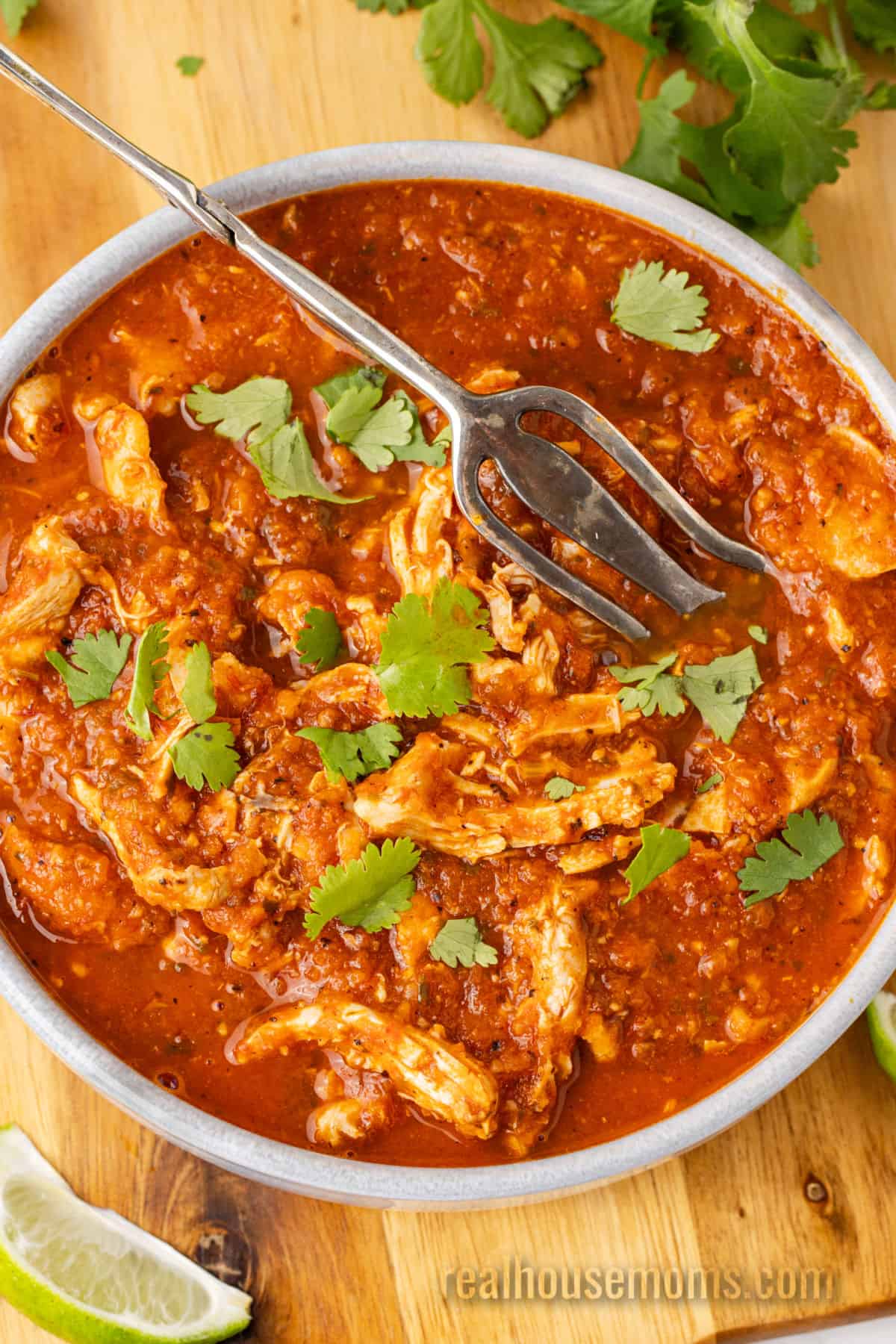 slow cooker chicken tinga in a serving bowl with chopped cilantro and a serving fork
