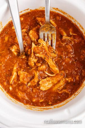 two forks resting in a crock pot after shredded the chicken thighs in tinga sauce
