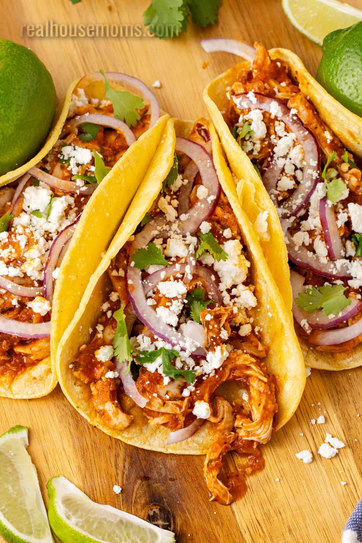 three chicken tinga tacos on a cutting board next to lime wedges