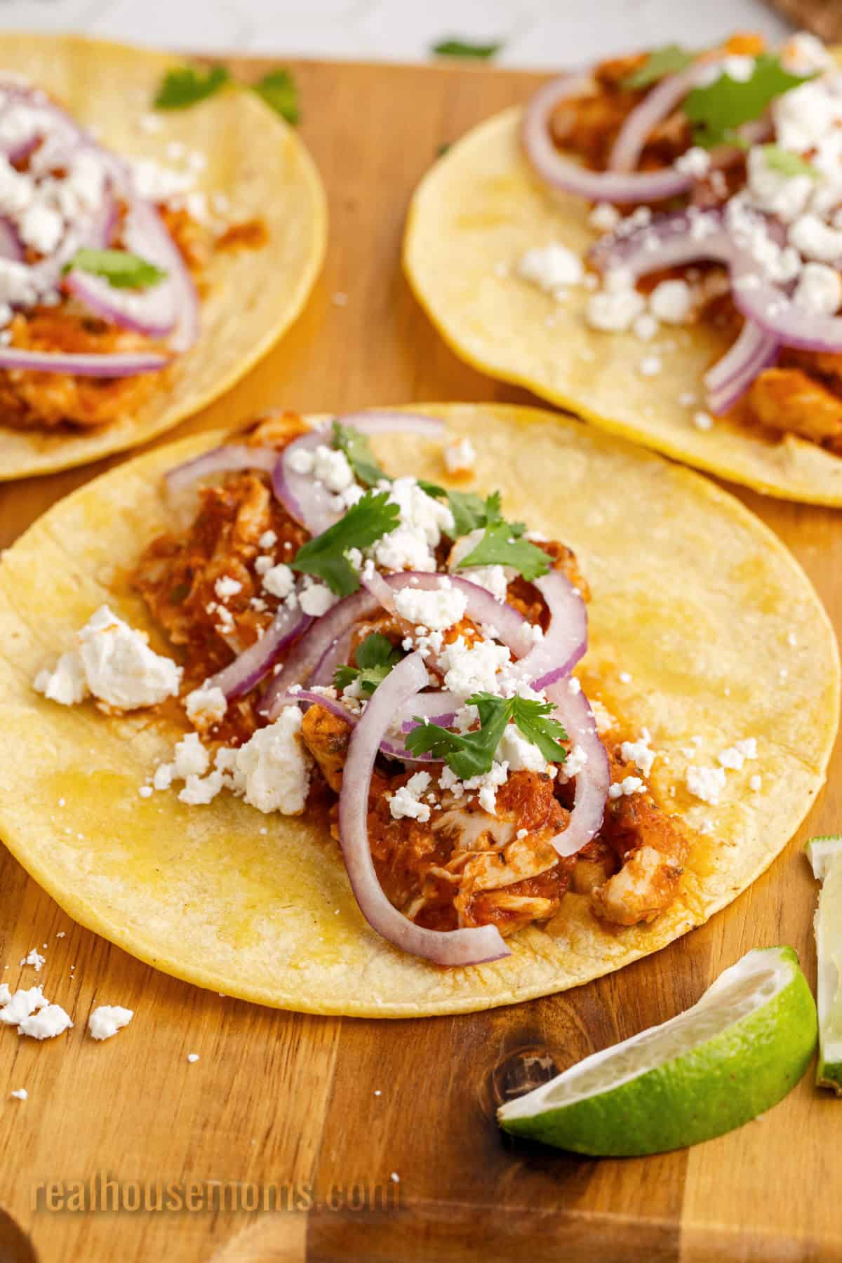 three chicken tinga tacos on a cutting board next to lime wedges